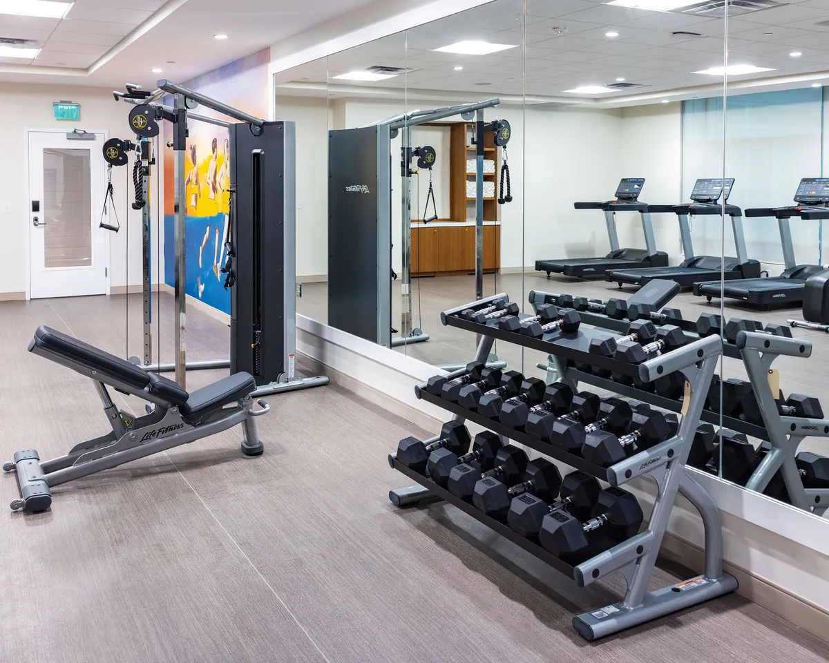 The resort's fitness center, filled with modern exercise equipment like treadmills, weight benches, and a range of free weights, is shown in a bright, mirrored room. The space is inviting and easily accessible for guests of all ages and fitness levels, allowing for both solo and group activities.