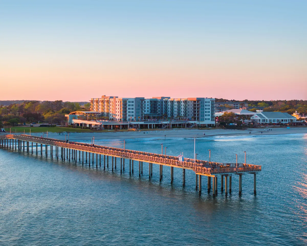 This image shows a tranquil scene with a pier extending over the water, neighboring buildings, and the distant horizon. The calm mood and open view evoke the peacefulness and connection to the Atlantic Ocean that a private balcony offers.