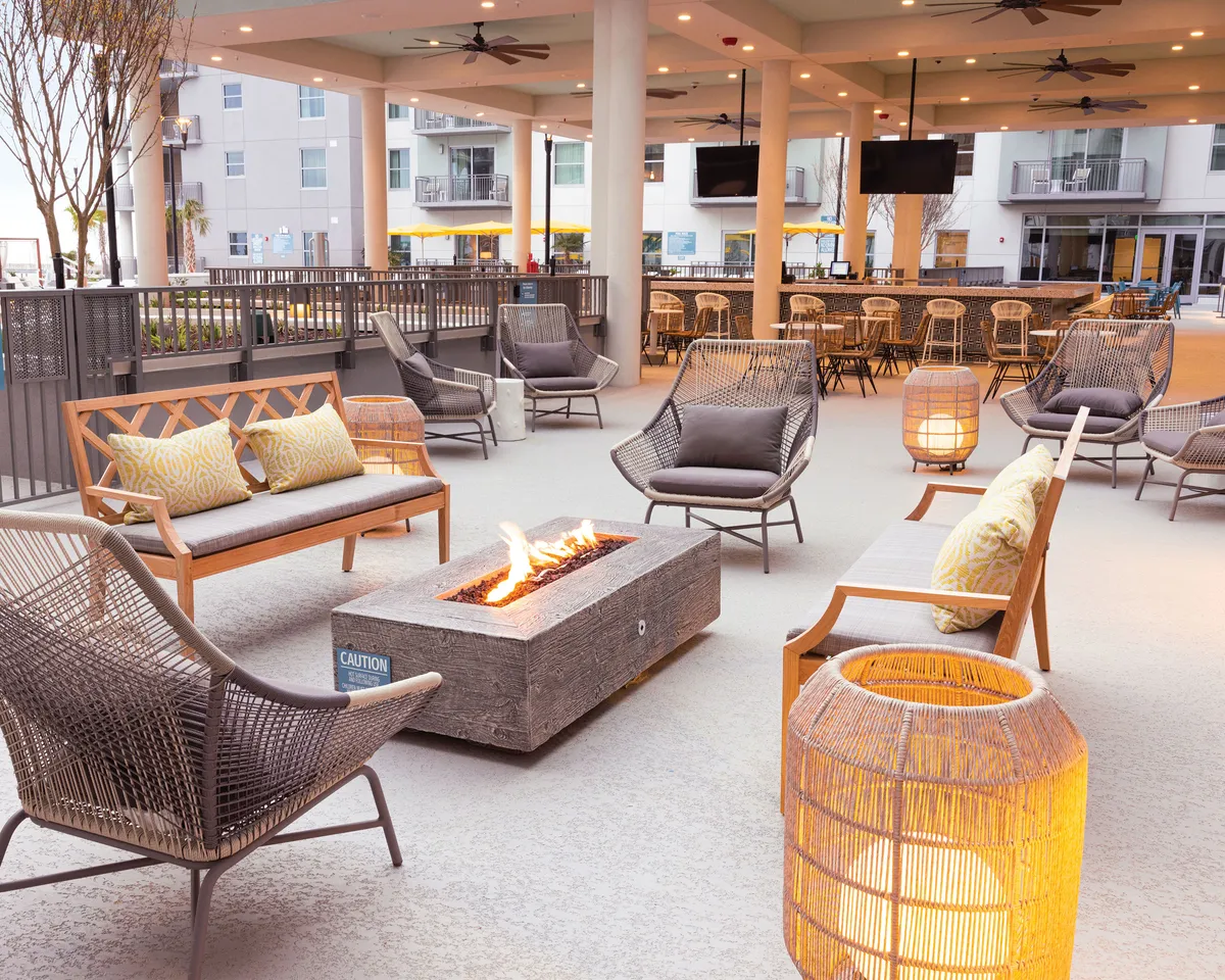 This cozy outdoor setting features a modern fire pit surrounded by comfortable seating and decorative lanterns. The area is designed for intimate gatherings, with guests relaxing and enjoying evening conversations under the warm glow of sunset.